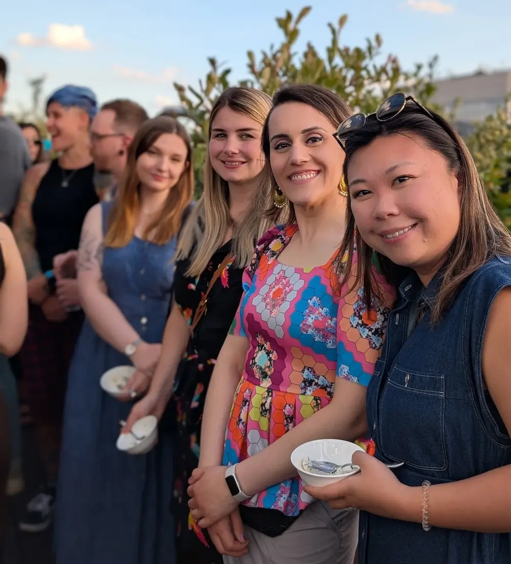 Four women smiling at an outdoor gathering, each holding a bowl.